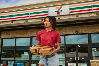 Person walking out of a 7-Eleven store with pizza boxes.