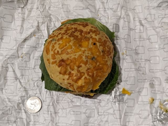 Wendy's Loaded Nacho Cheeseburger top-down view of bun with quarter for size comparison.